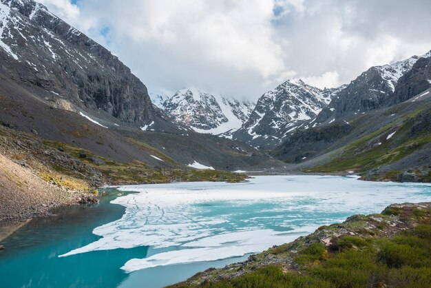 Paesaggio atmosferico dell'altopiano con lago alpino ghiacciato e alte montagne innevate Scenario fantastico con lago di montagna ghiacciato sullo sfondo di grandi montagne innevate tra nuvole basse Vista panoramica sul lago ghiacciato