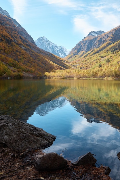 Paesaggio autunnale nel lago di montagna con acqua limpida alberi dorati sui pendii della riva di pietra delle montagne