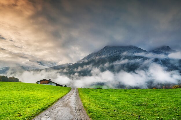 Paesaggio con strada, campo verde e montagne tra le nuvole