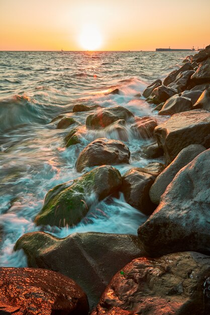 Paesaggio costiero con la calda luce della sera quando le onde si infrangono sulle rocce ricoperte di alghe