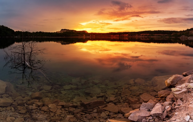 Paesaggio del cielo al tramonto su un lago con una riva di pietra.