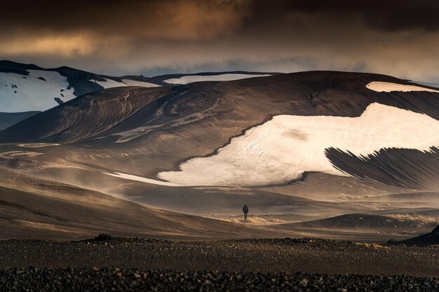 Paesaggio del viaggiatore uomo che cammina nella polverosa montagna vulcanica sugli altopiani islandesi in estate a Landmannalaugar