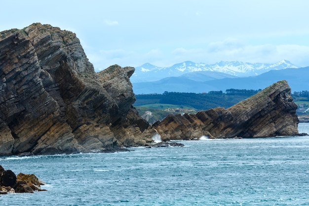 Paesaggio della costa rocciosa dell'Oceano Atlantico (Spagna) e montagne con neve sullo sfondo.