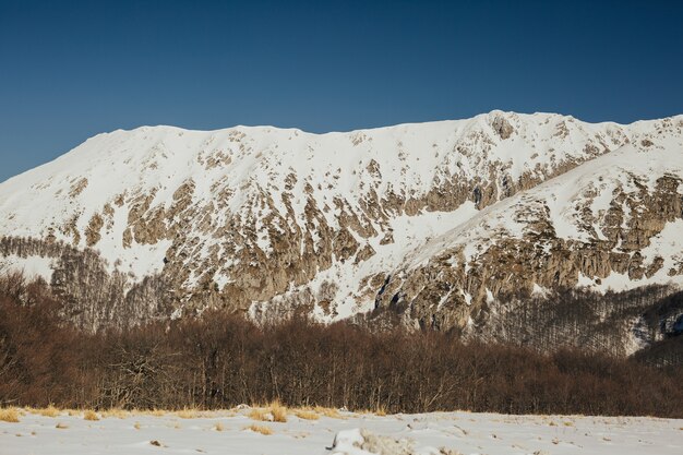 Paesaggio delle montagne rocciose ricoperte di neve con cielo blu sullo sfondo.