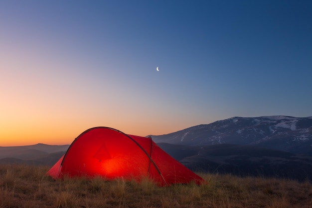 Paesaggio di alba con tenda luminosa di fronte al crinale della montagna contro il cielo colorato Caucaso Russia