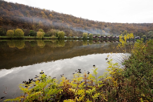 Paesaggio di campagna Case in legno con fumo sul lago Riflessi di un edificio nell'acqua in una giornata autunnale