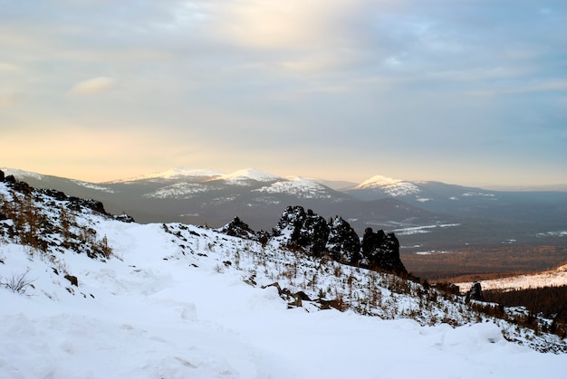 Paesaggio di montagna invernale degli Urali settentrionali durante l'alba con rocce in primo piano e picchi illuminati dal sole sullo sfondo