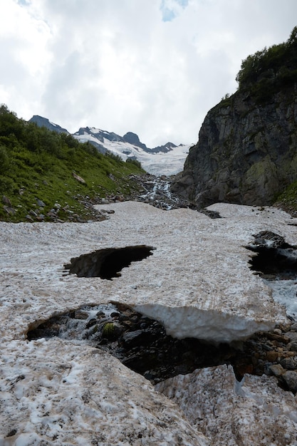 Paesaggio di montagna, neve che si scioglie, ghiacciaio e ruscello di montagna, grotte nel ghiaccio