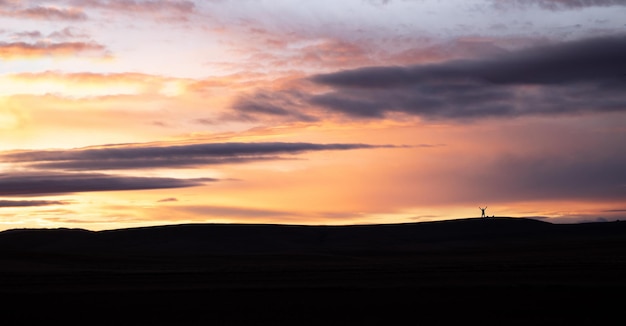 Paesaggio di montagne al tramonto con silhouette di scalatore che celebra la cima