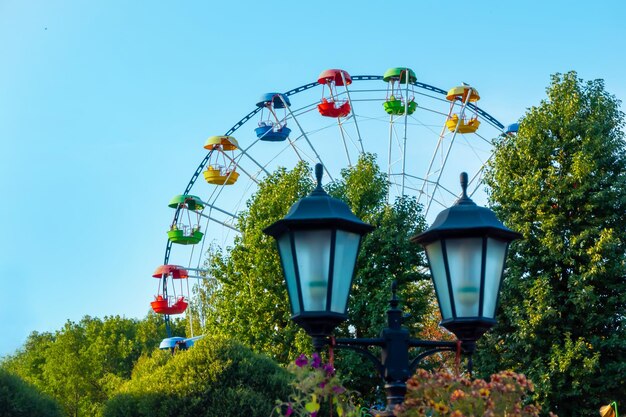 Paesaggio di un parco divertimenti con lanterna decorata con fiori sullo sfondo la parte superiore di una ruota panoramica che mostra sopra le cime degli alberi contro un cielo