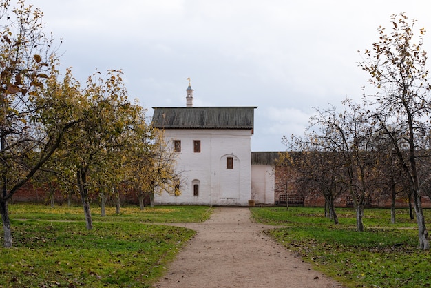 Paesaggio di una vecchia casa di mattoni bianchi in un giardino di mele dietro un grande vecchio recinto di mattoni. Autunno nuvoloso giorno