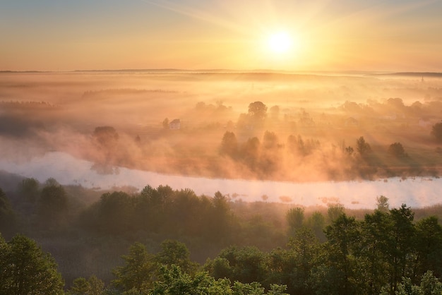 Paesaggio estivo con nebbia sul fiume. I primi raggi del sole nascente dipingono la nebbia