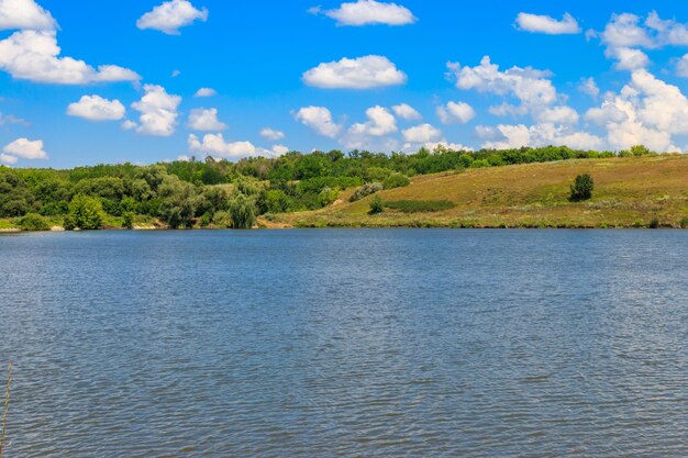 Paesaggio estivo con splendidi prati verdi lago, colline, alberi e cielo blu