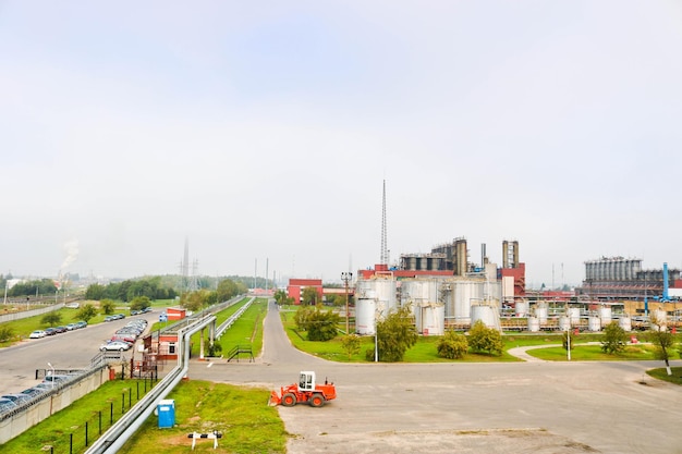 Paesaggio industriale con tubi e colonne di impianti chimici Sotto c'è un trattore arancione Il fumo proviene dal reattore Vista panoramica della produzione di riparazione Tubi di processo