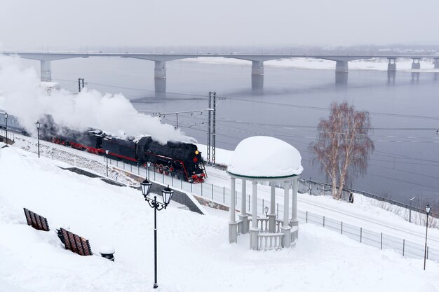 Paesaggio innevato invernale con locomotiva a vapore che si muove lungo la sponda del fiume
