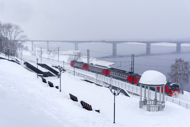 Paesaggio innevato invernale con treno elettrico multiplo che si muove lungo la sponda del fiume