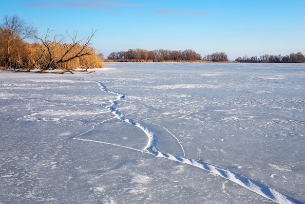 Paesaggio invernale con crepe, intoppo, canne e fiume ghiacciato