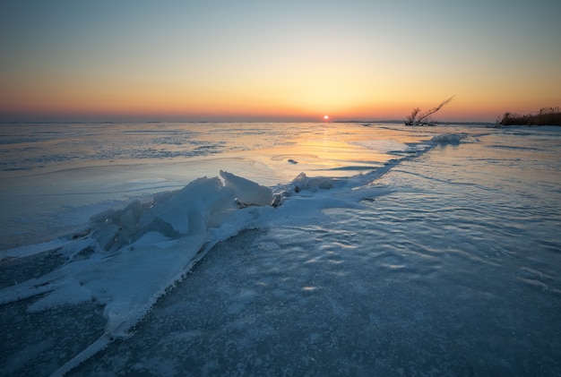 Paesaggio invernale con crepe sul lago ghiacciato vicino alla riva al tramonto