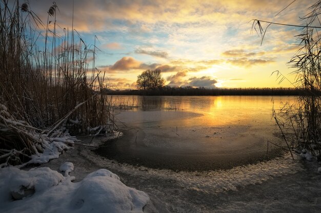 Paesaggio invernale con fiume ghiacciato e cielo al tramonto
