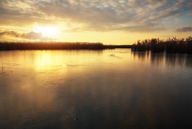 Paesaggio invernale con fiume ghiacciato e cielo al tramonto