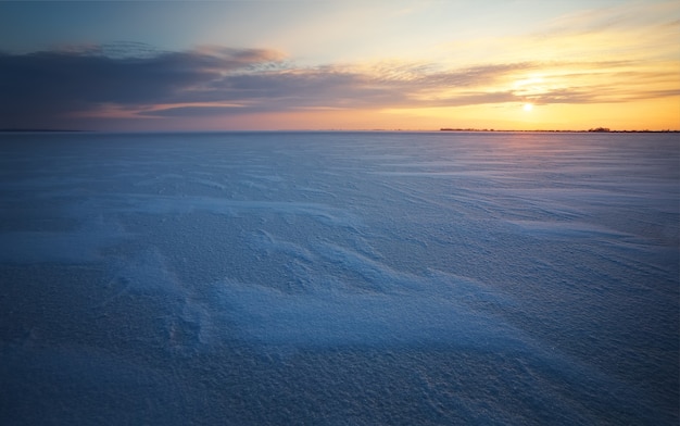 Paesaggio invernale con lago ghiacciato e cielo al tramonto.