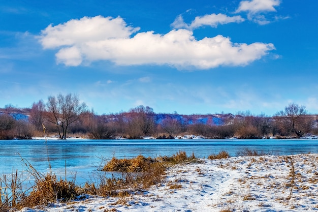 Paesaggio invernale con un fiume e una bella nuvola bianca nel cielo blu