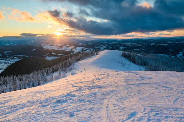 Paesaggio invernale serale in montagna con foresta di abeti al tramonto Colline innevate dopo forti nevicate Paesaggio innevato di piste da sci Orizzonte drammatico di nuvole all'alba