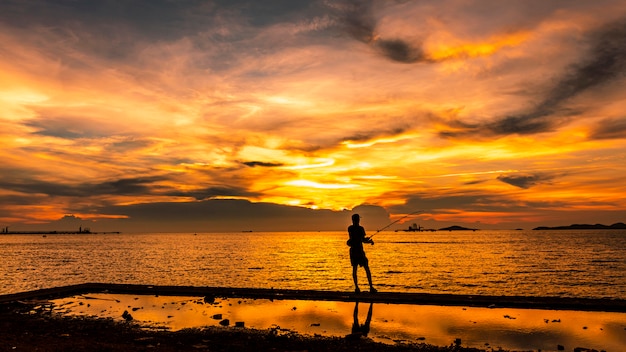 Paesaggio marino di Twilight il tramonto e l&#39;oro chiaro con la priorità alta della siluetta del pescatore