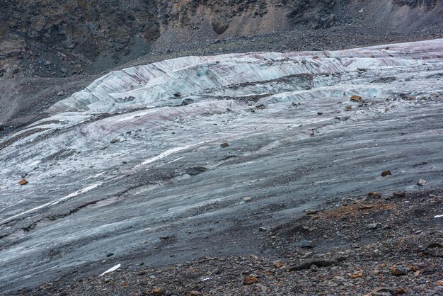 Paesaggio montano atmosferico con lunga lingua di ghiacciaio con crepaccio e cascata di ghiaccio primo piano Struttura naturale con pietre arancioni su ghiaccio glaciale incrinato Sfondo naturale con bellissimo ghiacciaio sulle rocce