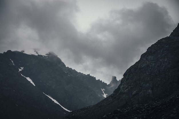 Paesaggio montano atmosferico scuro con picco roccioso appuntito nero nel cielo nuvoloso grigio.