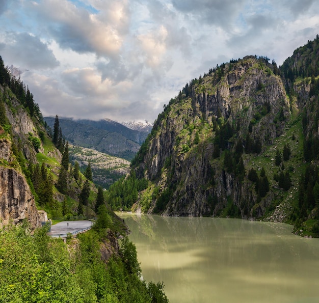 Paesaggio montano delle Alpi estive con lago artificiale torbido e ripidi pendii rocciosi Svizzera