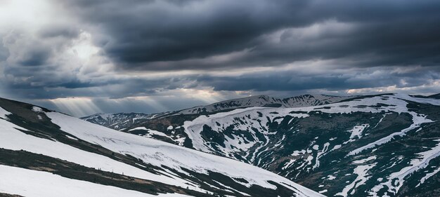 Paesaggio montano primaverile con neve, vista panoramica. Nuvole drammatiche che si trovano all'orizzonte e il sole splende. Sfondo naturale di viaggio all'aperto in stile retrò hipster.