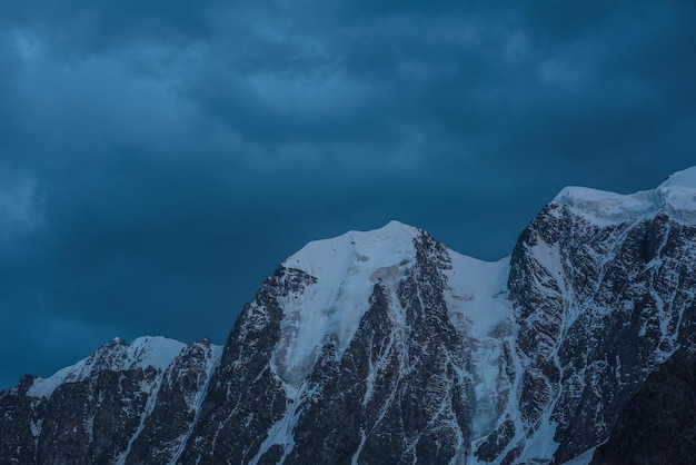 Paesaggio notturno atmosferico con enormi cime innevate in un cielo drammatico ghiacciaio e cornice appesi su bellissime montagne giganti di neve di notte alta catena montuosa innevata al crepuscolo alla luce fioca