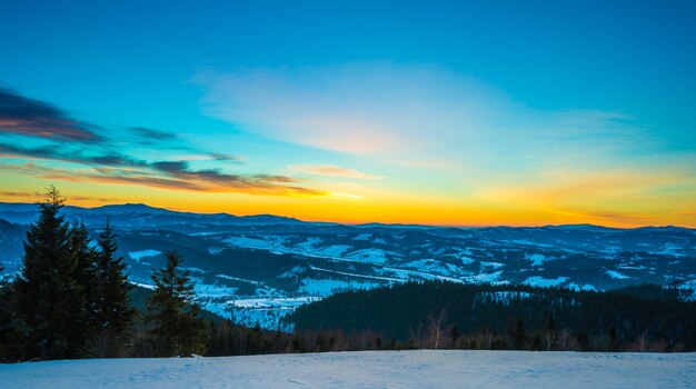 Paesaggio pacificante nella valle di montagna con foresta di abeti rossi e cumuli di neve sullo sfondo di nessun tramonto e cielo blu con nuvole. Concetto di attività ricreative all'aperto. Spazio pubblicitario