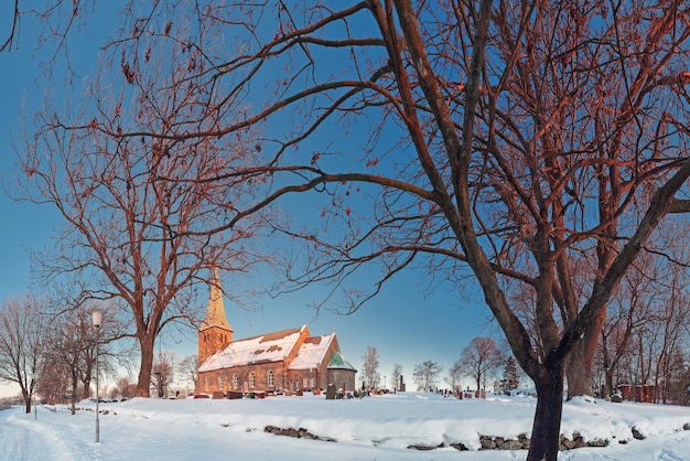 Paesaggio panoramico invernale con una chiesa di campagna norvegese e un cimitero al tramonto