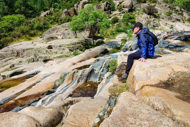 Paesaggio roccioso con cascate e uomo seduto su una roccia in appoggio