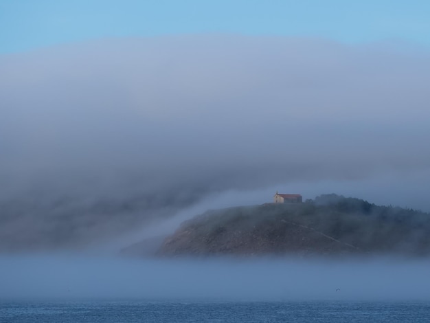 Paesaggio tra nuvole basse dove si vede una chiesa su un monte e il mare.