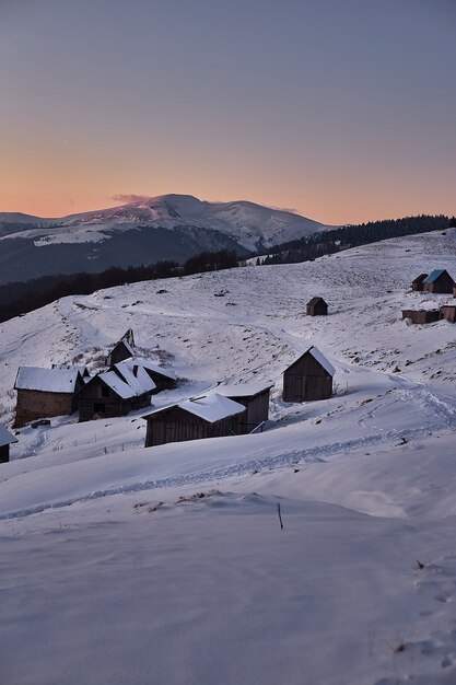 Paesaggio tramonto invernale con case in legno in montagne innevate