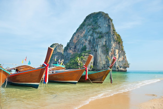 Paesaggio tropicale con fila di barche tradizionali tailandesi a coda lunga sulla spiaggia di sabbia con acqua limpida e isola rocciosa sullo sfondo