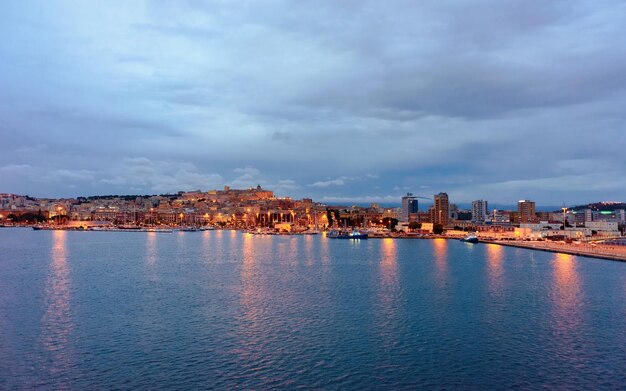 Paesaggio urbano con la città vecchia e il porto sardo con navi nel Mar Mediterraneo vicino a Cagliari, nell'isola del sud Sardegna in Italia in estate. Vista sul porto turistico della città con yacht e barche. Al crepuscolo