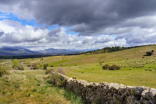 Paesaggio verde con cielo drammatico e recinzione in pietra naturale che separa i prati erbosi. Madrid.