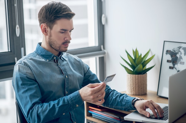 Pagamenti online. Giovane uomo in camicia di jeans che effettua pagamenti periodici online