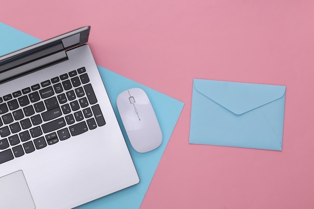 Pagamento online. Computer portatile con mouse per pc, busta su sfondo rosa pastello blu. Vista dall'alto.