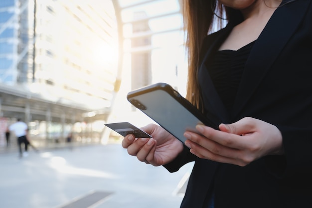 Pagamento online, le mani della donna che tengono una carta di credito e utilizzano lo smartphone per lo shopping online.