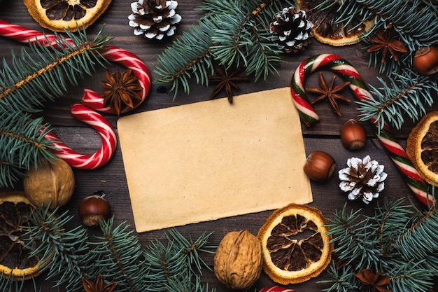 Pagina delle noci di canna del caramello delle arance dei coni dell'albero di Natale su fondo di legno scuro. Copia spazio. Disteso. Vecchia carta per il testo.