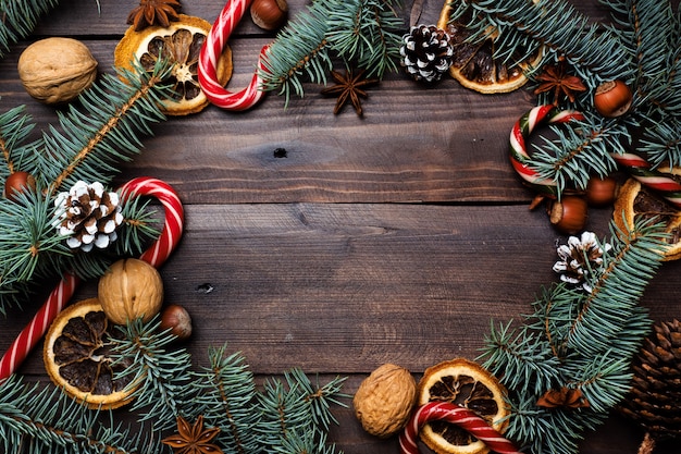 Pagina delle noci di canna del caramello delle arance dei coni dell'albero di Natale su fondo di legno scuro. Copia spazio. Disteso.