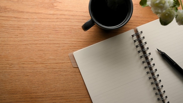 Pagina in bianco del taccuino con la penna, la tazza di caffè e lo spazio sul fondo della tavola di legno. colpo dall'alto