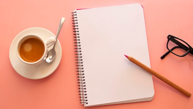Pagina vuota di un taccuino accanto a un computer portatile e una tazza bianca con caffè su sfondo rosa chiaro