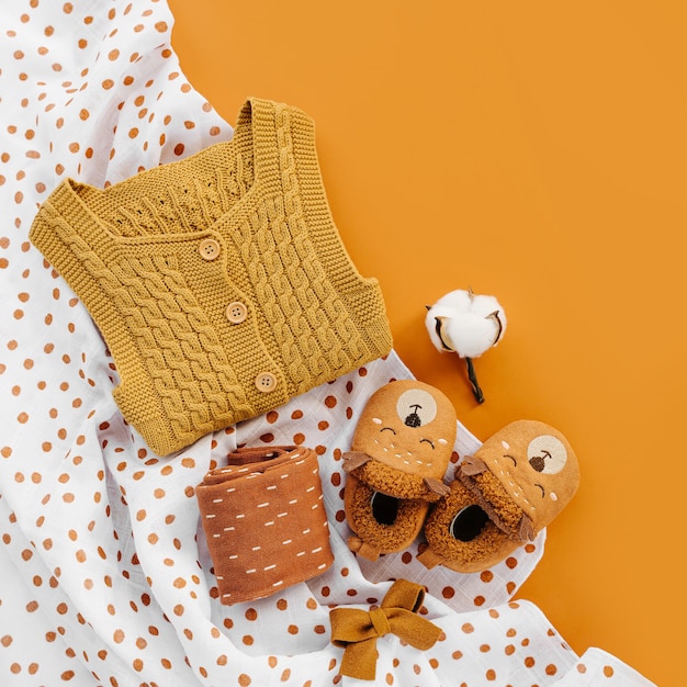 Pagliaccetto giallo lavorato a maglia, calzini e simpatiche pantofole per bambini con coperta in mussola. Set di vestiti e accessori per neonati. Disposizione piatta, vista dall'alto