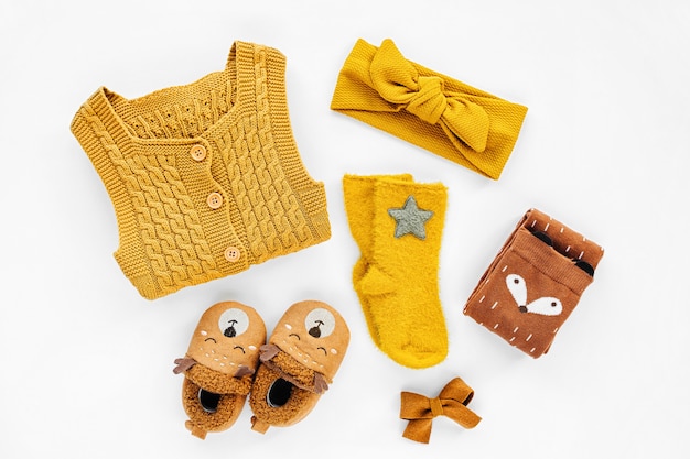 Pagliaccetto giallo lavorato a maglia, fascia per capelli, calzini e simpatiche pantofole per bambini. Set di vestiti e accessori per neonati. Disposizione piatta, vista dall'alto